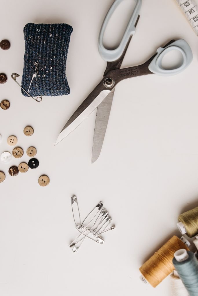 Top view of sewing tools including scissors, buttons, and threads on a white surface.