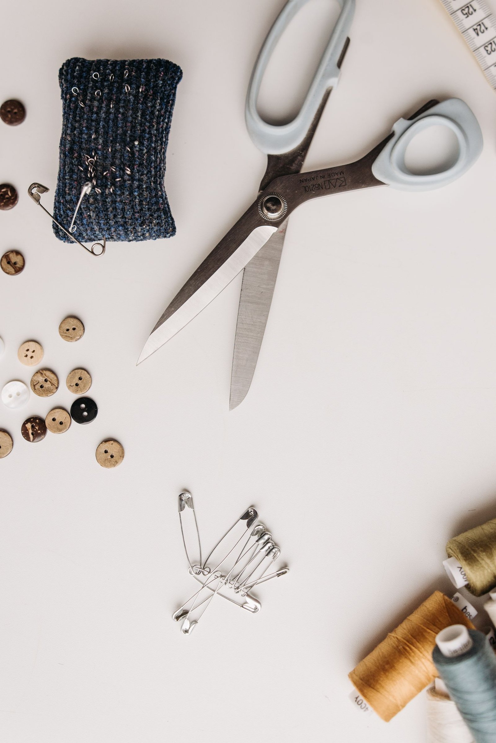 Top view of sewing tools including scissors, buttons, and threads on a white surface.